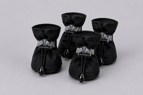Set of four black Pawro waterproof dog boots with reflective straps and elastic drawstrings, on a grey background