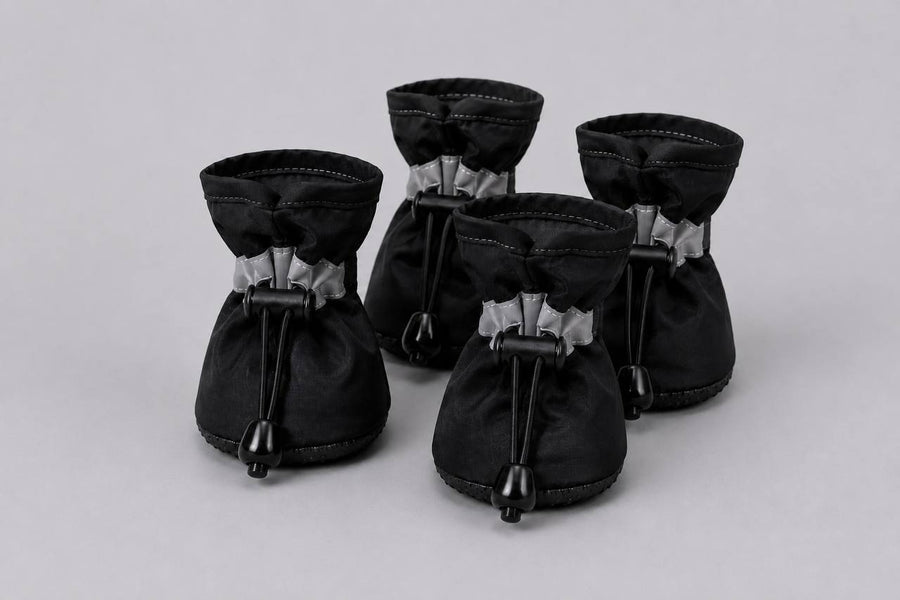 Set of four black Pawro waterproof dog boots with reflective straps and elastic drawstrings, on a grey background